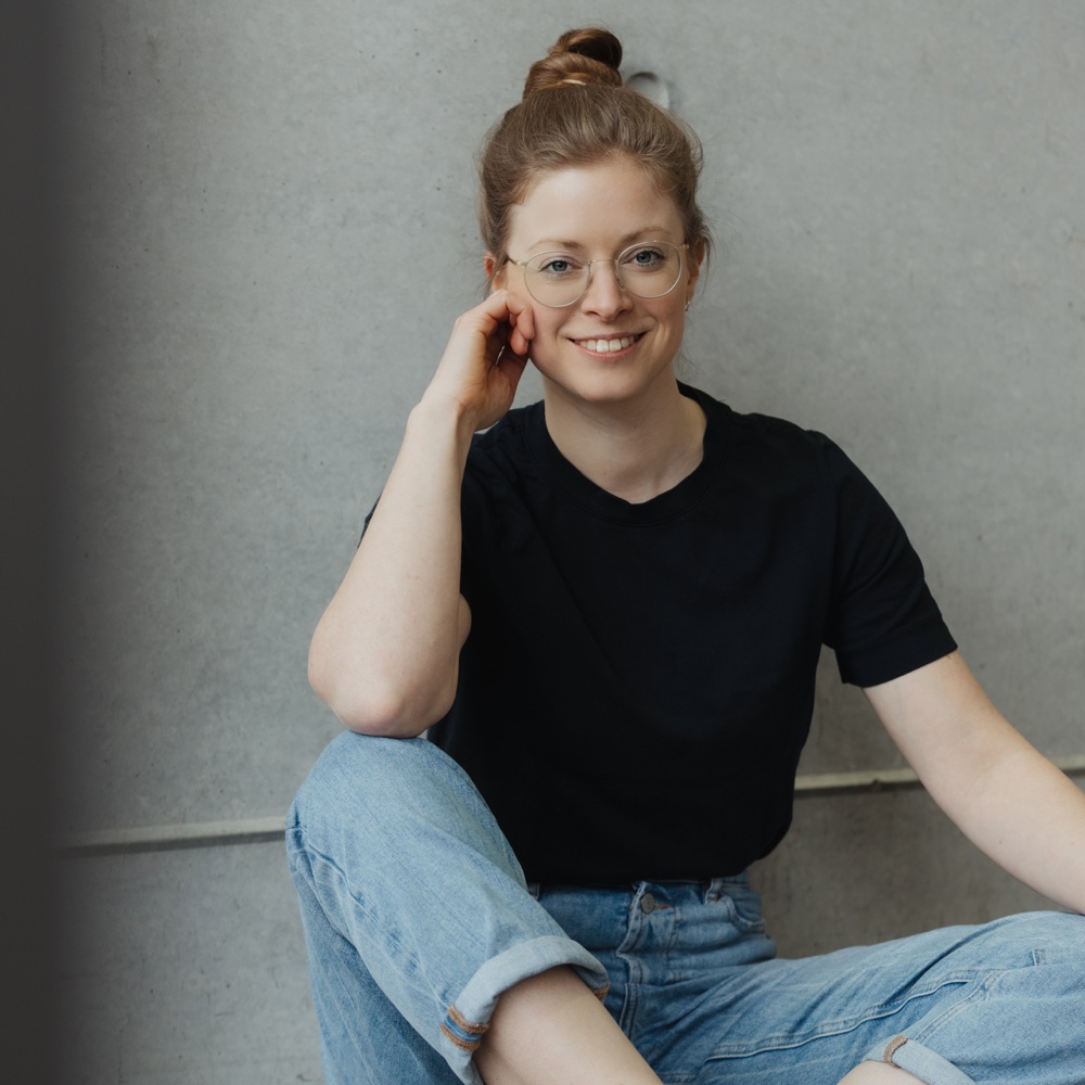 Porträt von Verena Gerardy, die lächelnd auf dem Boden sitzt